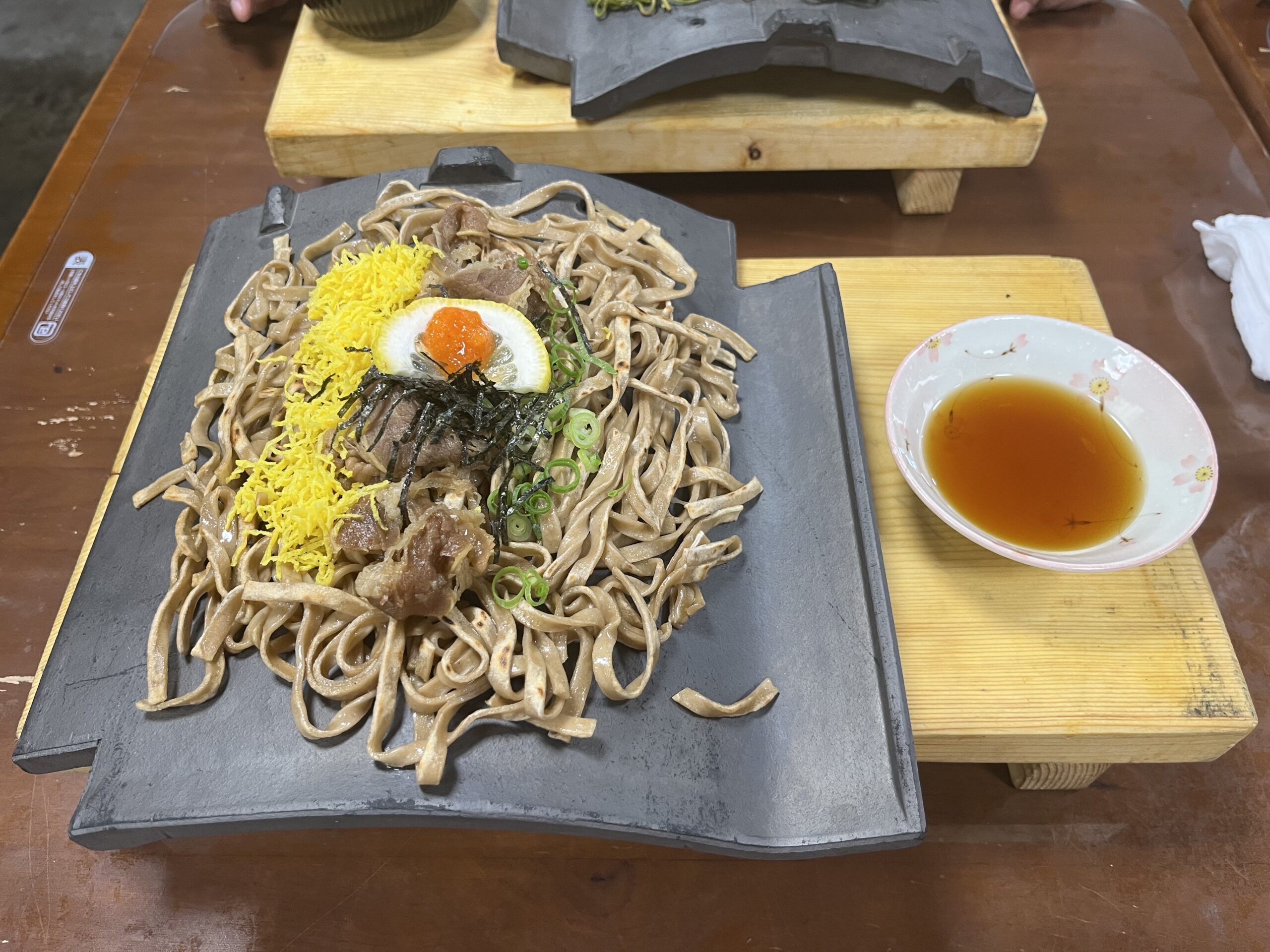 瓦に盛られたそばと錦糸卵、肉、海苔、レモン